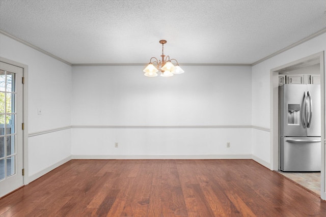 unfurnished dining area with an inviting chandelier, ornamental molding, a textured ceiling, wood finished floors, and baseboards