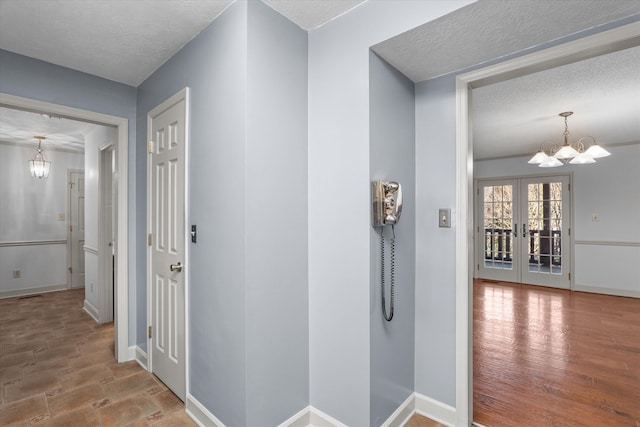 hall featuring baseboards, a chandelier, a textured ceiling, and french doors