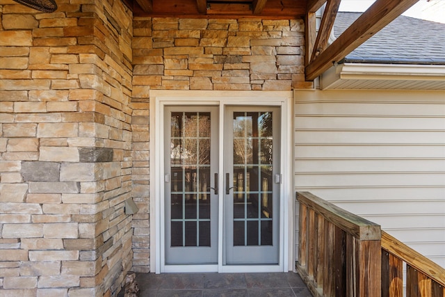 property entrance featuring stone siding, french doors, and roof with shingles