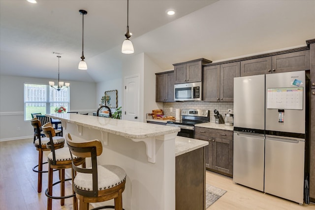 2613 Inverness Dr, Hephzibah, GA 30815 - kitchen with stainless steel appliances, dark brown cabinetry, light wood finished floors, a kitchen island with sink, and lofted ceiling