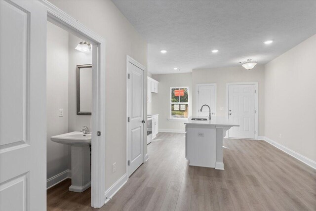 kitchen with sink, an island with sink, light hardwood / wood-style floors, a kitchen bar, and white cabinetry