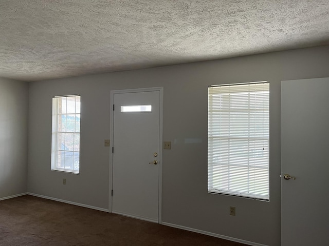 foyer featuring dark carpet and a textured ceiling