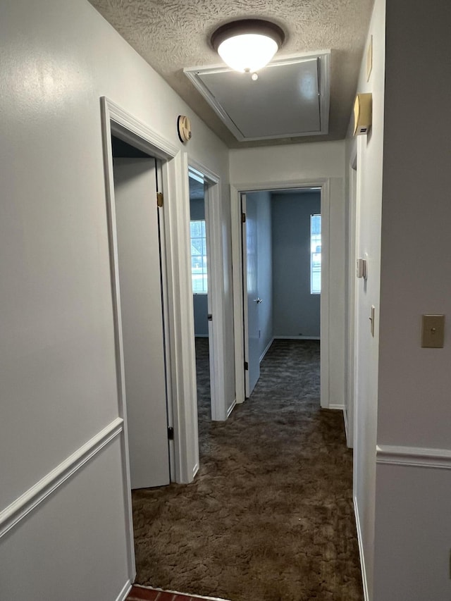 hall with dark colored carpet, plenty of natural light, and a textured ceiling