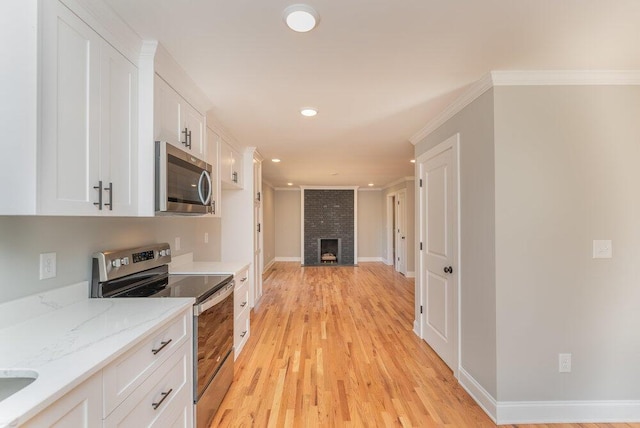 kitchen featuring white cabinets, ornamental molding, a fireplace, light stone counters, and stainless steel appliances