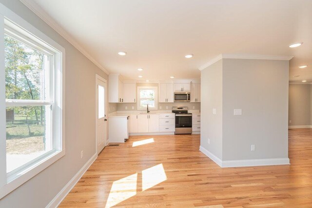 kitchen featuring light wood-type flooring, stainless steel appliances, crown molding, sink, and white cabinets