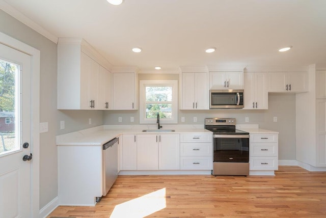 kitchen with light wood-type flooring, ornamental molding, stainless steel appliances, sink, and white cabinets