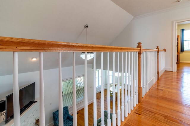 hallway with baseboards, ornamental molding, light wood finished floors, and lofted ceiling