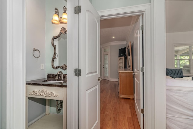 hallway featuring crown molding, a sink, light wood finished floors, and baseboards