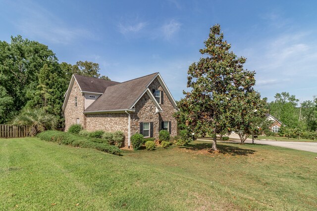 view of front of home featuring fence, roof with shingles, a front lawn, stone siding, and brick siding
