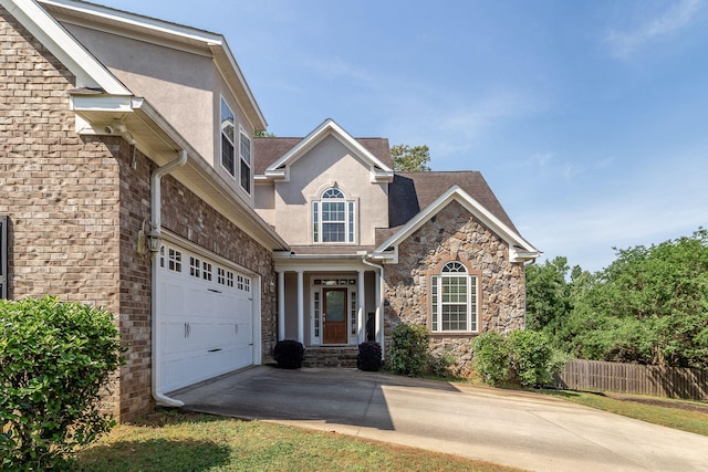 traditional-style house featuring fence, stucco siding, driveway, and stone siding