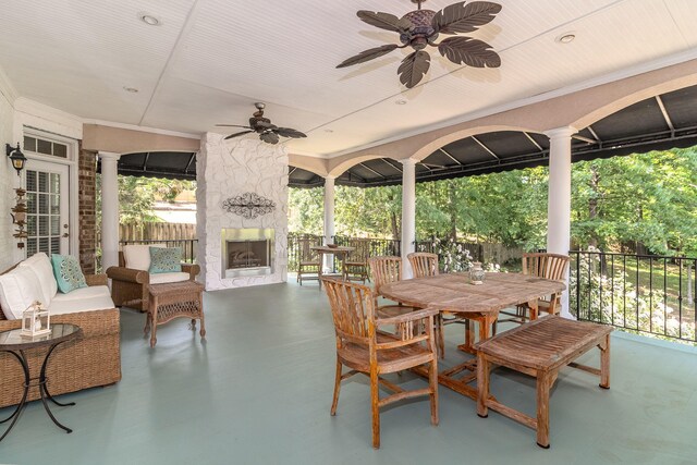 view of patio with fence, a ceiling fan, an outdoor living space with a fireplace, and outdoor dining space