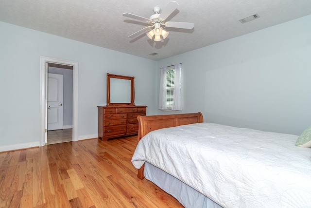 bedroom with visible vents, baseboards, light wood-type flooring, a textured ceiling, and a ceiling fan