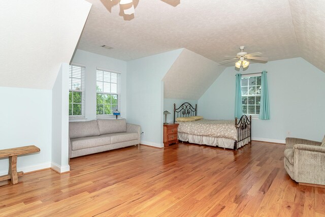 bedroom featuring a textured ceiling, multiple windows, lofted ceiling, and light wood-style floors