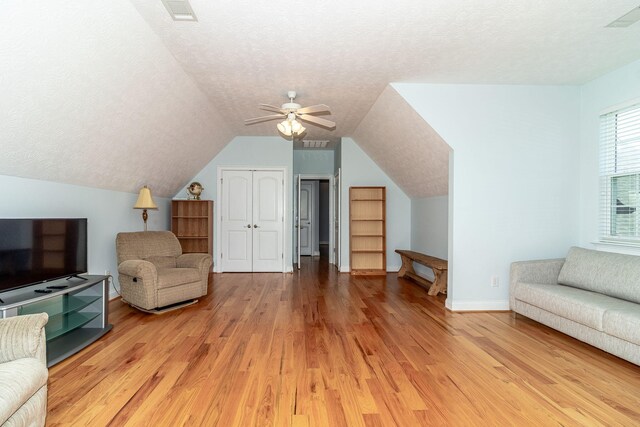 interior space with ceiling fan, a textured ceiling, visible vents, light wood finished floors, and lofted ceiling