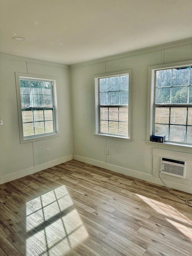 unfurnished room featuring crown molding, a wealth of natural light, a wall unit AC, and light wood-type flooring