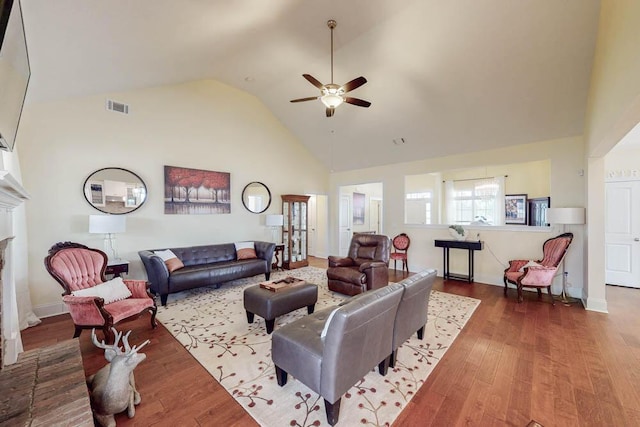 living room with visible vents, a brick fireplace, ceiling fan, wood finished floors, and high vaulted ceiling