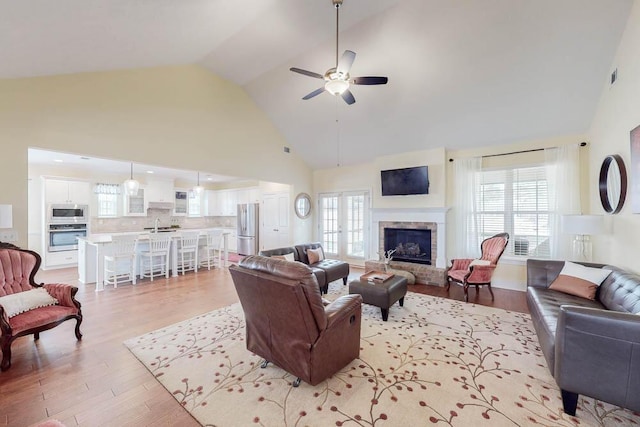 living area with visible vents, a fireplace, light wood-style floors, high vaulted ceiling, and a ceiling fan