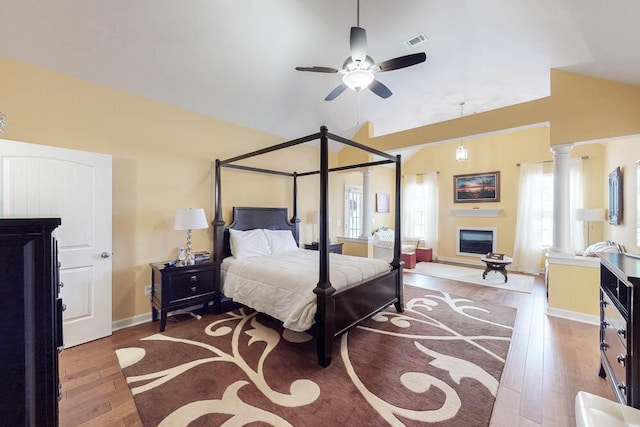 bedroom featuring visible vents, a glass covered fireplace, wood finished floors, baseboards, and vaulted ceiling