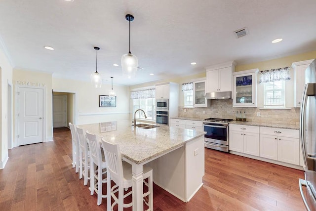 kitchen with tasteful backsplash, under cabinet range hood, appliances with stainless steel finishes, wood finished floors, and a sink