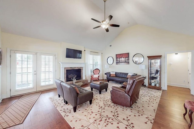 living area with high vaulted ceiling, a fireplace with raised hearth, light wood-style flooring, baseboards, and ceiling fan