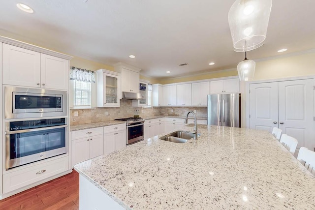 kitchen featuring a sink, under cabinet range hood, backsplash, white cabinetry, and appliances with stainless steel finishes