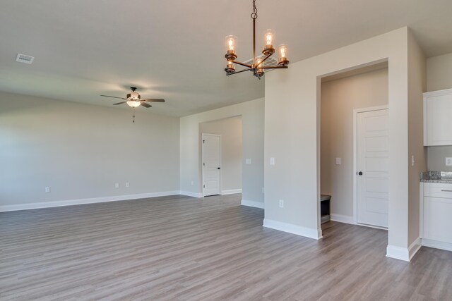 interior space with ceiling fan with notable chandelier, visible vents, light wood-style floors, and baseboards