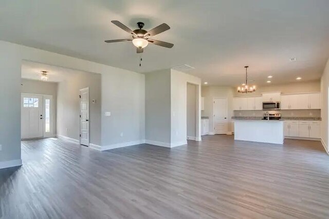 unfurnished living room featuring ceiling fan with notable chandelier, recessed lighting, wood finished floors, and baseboards