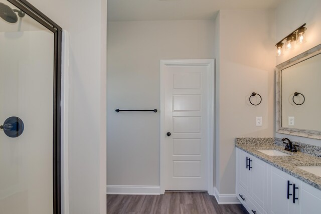 bathroom with a shower with door, baseboards, double vanity, wood finished floors, and a sink