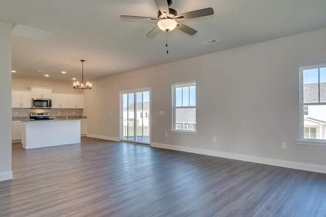 unfurnished living room featuring visible vents, plenty of natural light, baseboards, and ceiling fan with notable chandelier