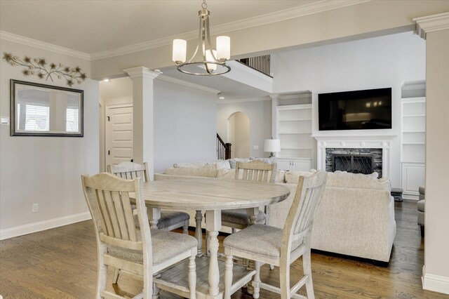 dining room featuring a stone fireplace, ornamental molding, dark wood-type flooring, and an inviting chandelier