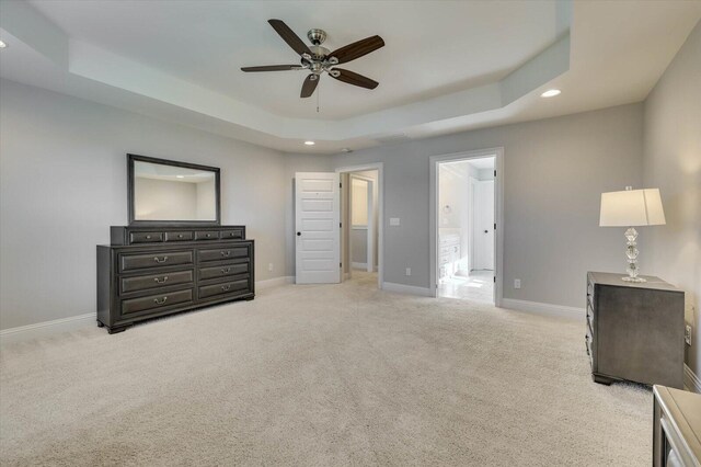 carpeted bedroom featuring a tray ceiling, connected bathroom, and ceiling fan