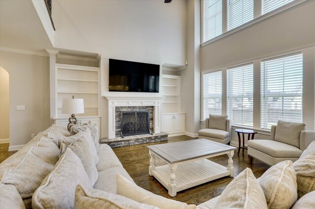 living room featuring built in shelves, dark hardwood / wood-style flooring, a stone fireplace, and a high ceiling