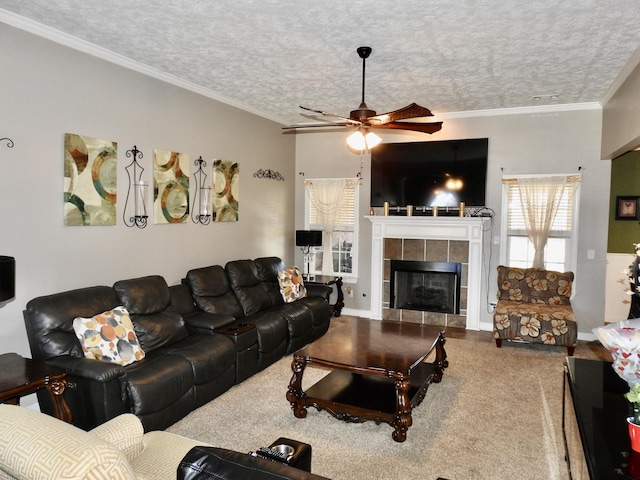 living room with ceiling fan, crown molding, a textured ceiling, and a tiled fireplace