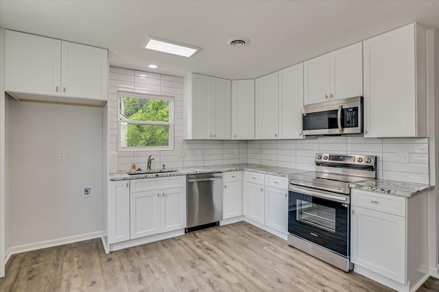 kitchen with a sink, light wood-style flooring, stainless steel appliances, tasteful backsplash, and visible vents