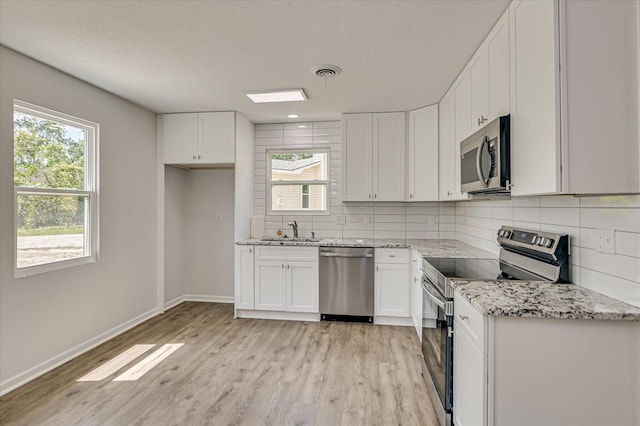 kitchen with white cabinets, a sink, stainless steel appliances, decorative backsplash, and light wood-type flooring
