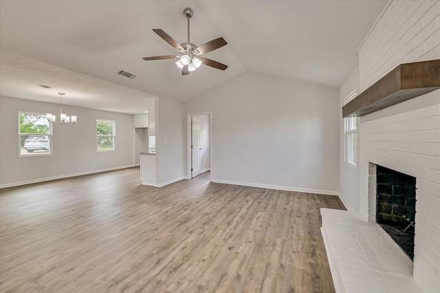 unfurnished living room featuring visible vents, a fireplace, vaulted ceiling, wood finished floors, and ceiling fan with notable chandelier