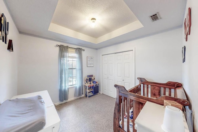 bedroom with a raised ceiling, a nursery area, a textured ceiling, and a closet