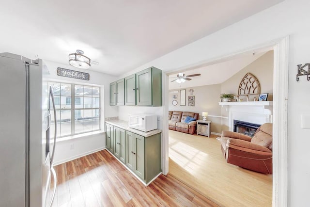 kitchen with light hardwood / wood-style flooring, ceiling fan, stainless steel fridge, and green cabinetry