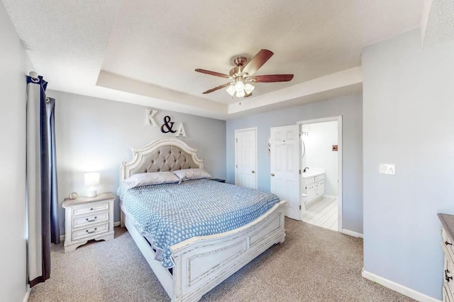 bedroom featuring light carpet, connected bathroom, a raised ceiling, and ceiling fan