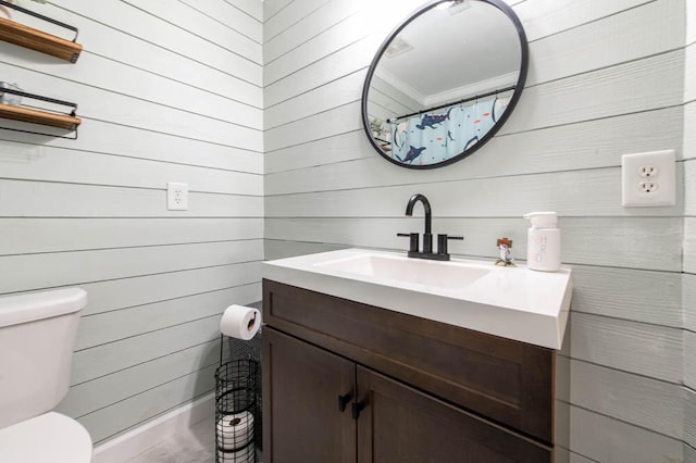 bathroom with vanity, wooden walls, and toilet