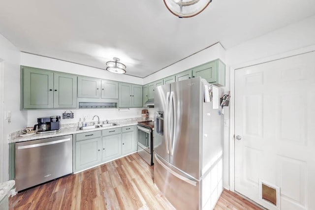 kitchen with appliances with stainless steel finishes, sink, light hardwood / wood-style floors, and green cabinetry