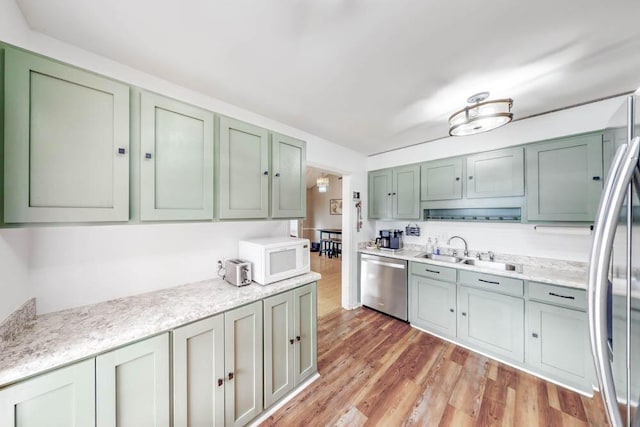 kitchen with sink, light hardwood / wood-style flooring, green cabinets, stainless steel appliances, and light stone countertops