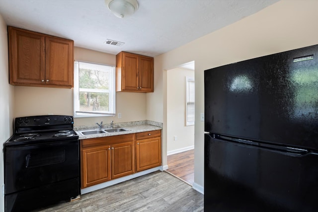 kitchen with sink, black appliances, and light hardwood / wood-style floors