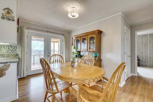 dining room with a textured ceiling, baseboards, light wood-style floors, french doors, and crown molding