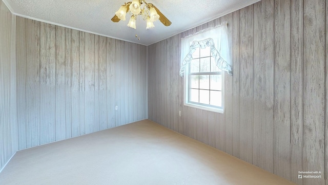 spare room with a textured ceiling, carpet floors, a ceiling fan, and wooden walls