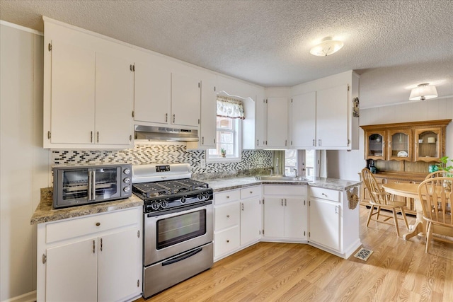 kitchen featuring under cabinet range hood, visible vents, white cabinetry, light wood-type flooring, and gas range