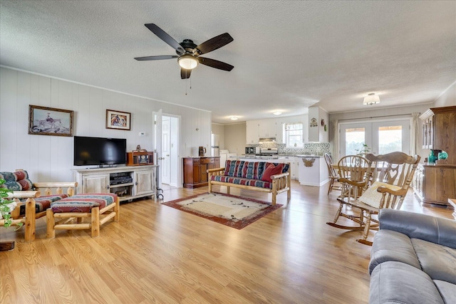 living room featuring light wood finished floors, a ceiling fan, a textured ceiling, and french doors