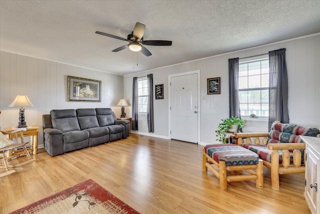 living room featuring light wood-type flooring, ceiling fan, baseboards, and a textured ceiling