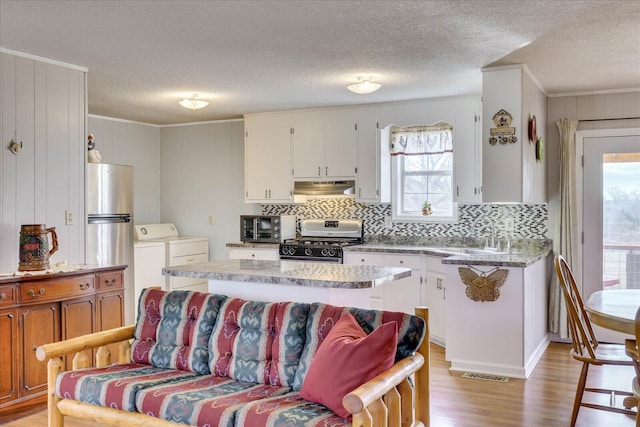 kitchen featuring freestanding refrigerator, washer and dryer, under cabinet range hood, a sink, and gas stove