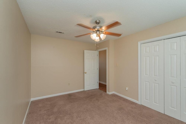 unfurnished bedroom featuring ceiling fan, a closet, light colored carpet, and a textured ceiling